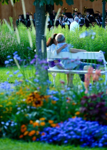 Couple enjoys a garden concert from a white bench