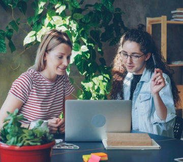 Two women collaborate at a laptop together.
