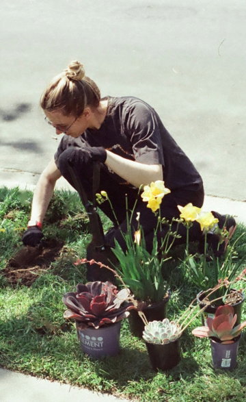a woman kneeling down in the grass next to a potted plant